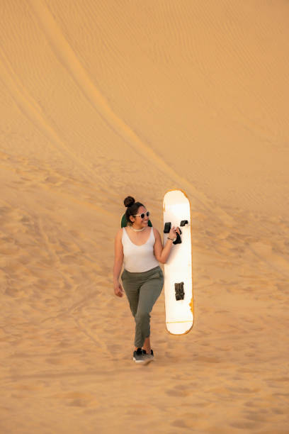 Young woman holding her sandboard high in excitement after a fun ride down the sand dunes in Huacachina, Ica, Peru.